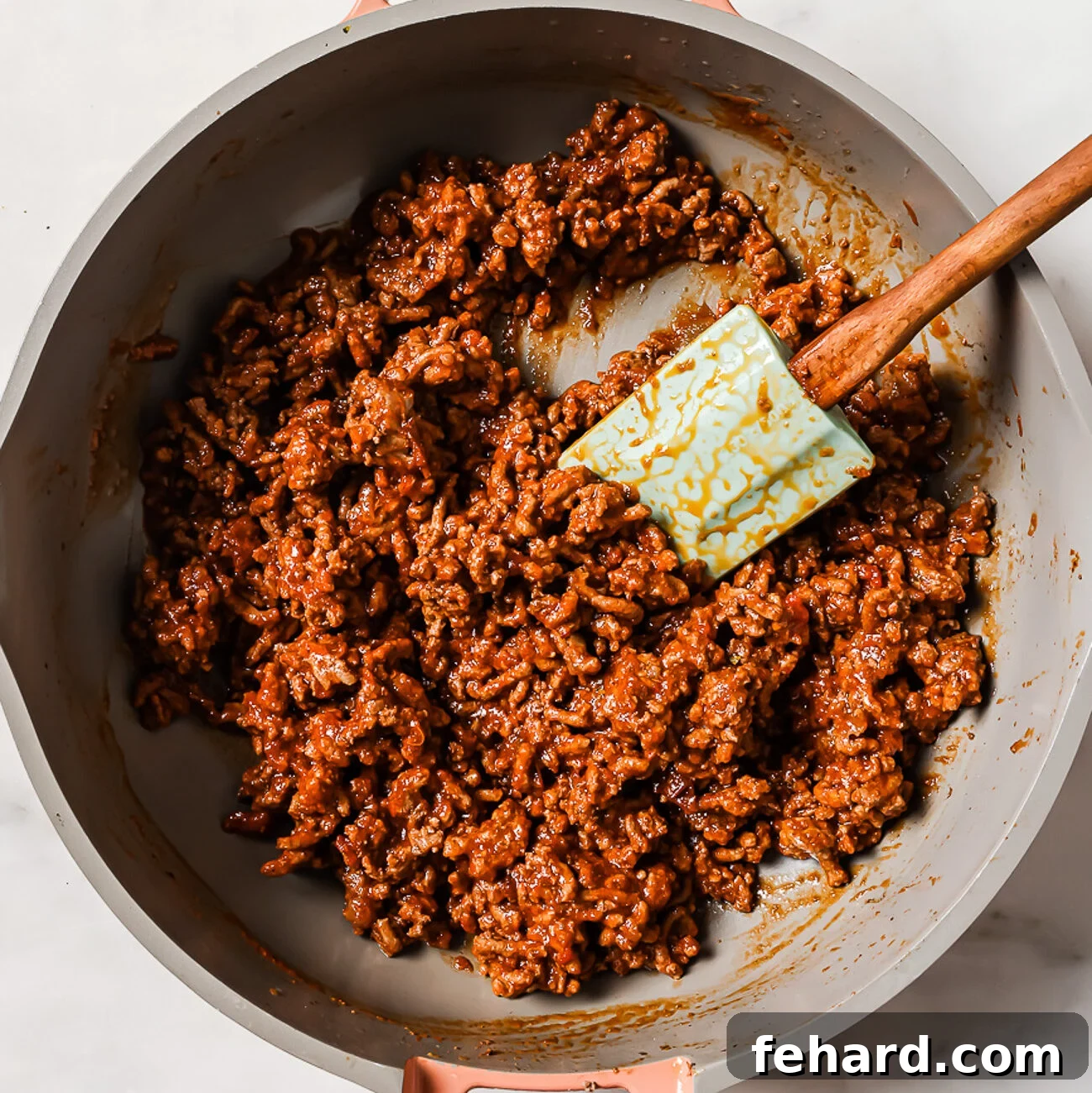 Ground beef simmering with tomato sauce and spices in a skillet, forming a moist and flavorful taco filling.