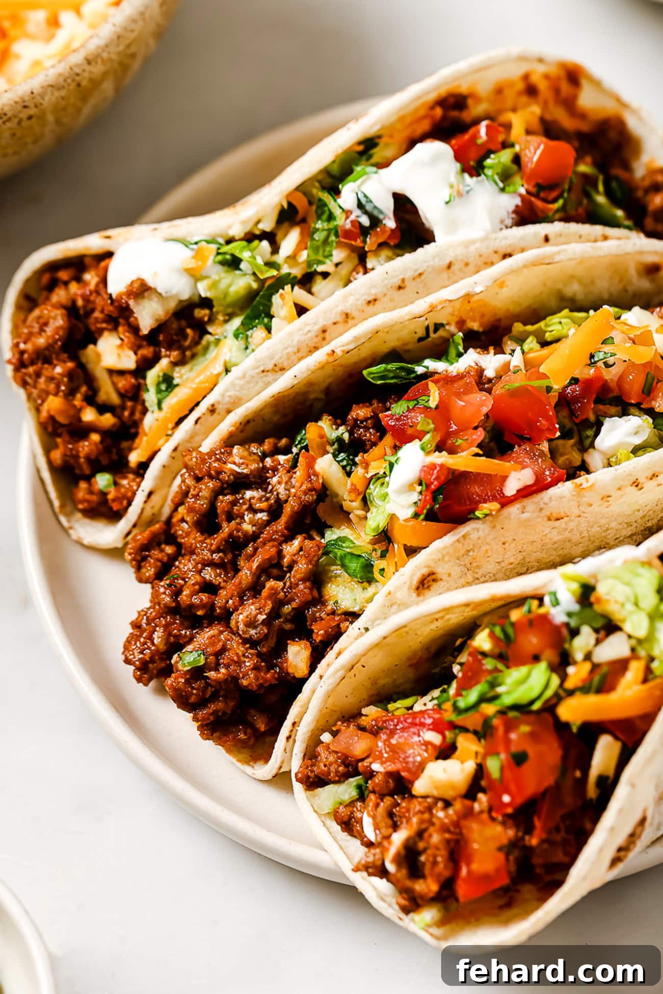 Three perfectly assembled ground beef tacos presented on a clean white plate, ready for dining.