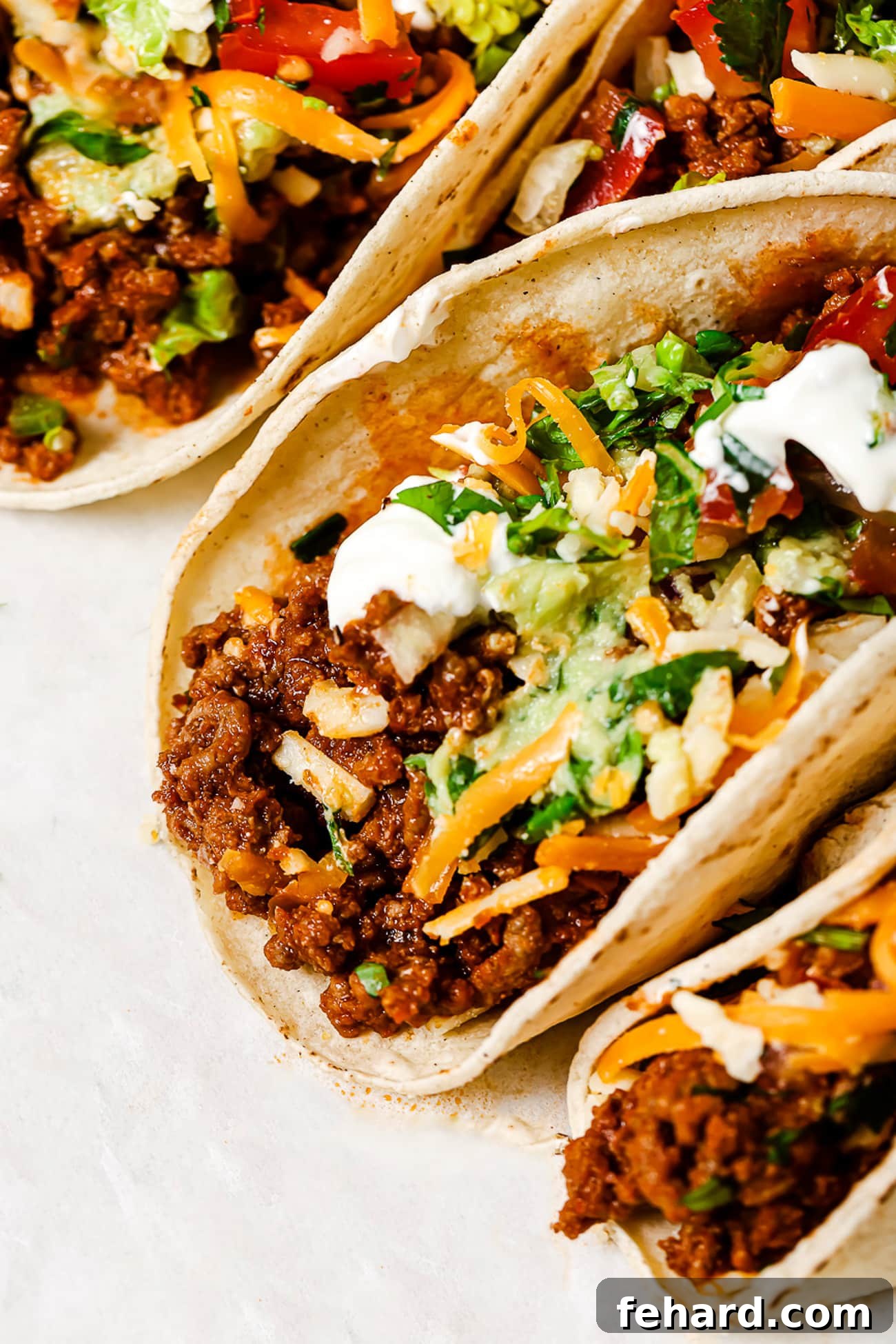 A closeup of ground beef tacos piled high with vibrant, colorful toppings, ready to be enjoyed.