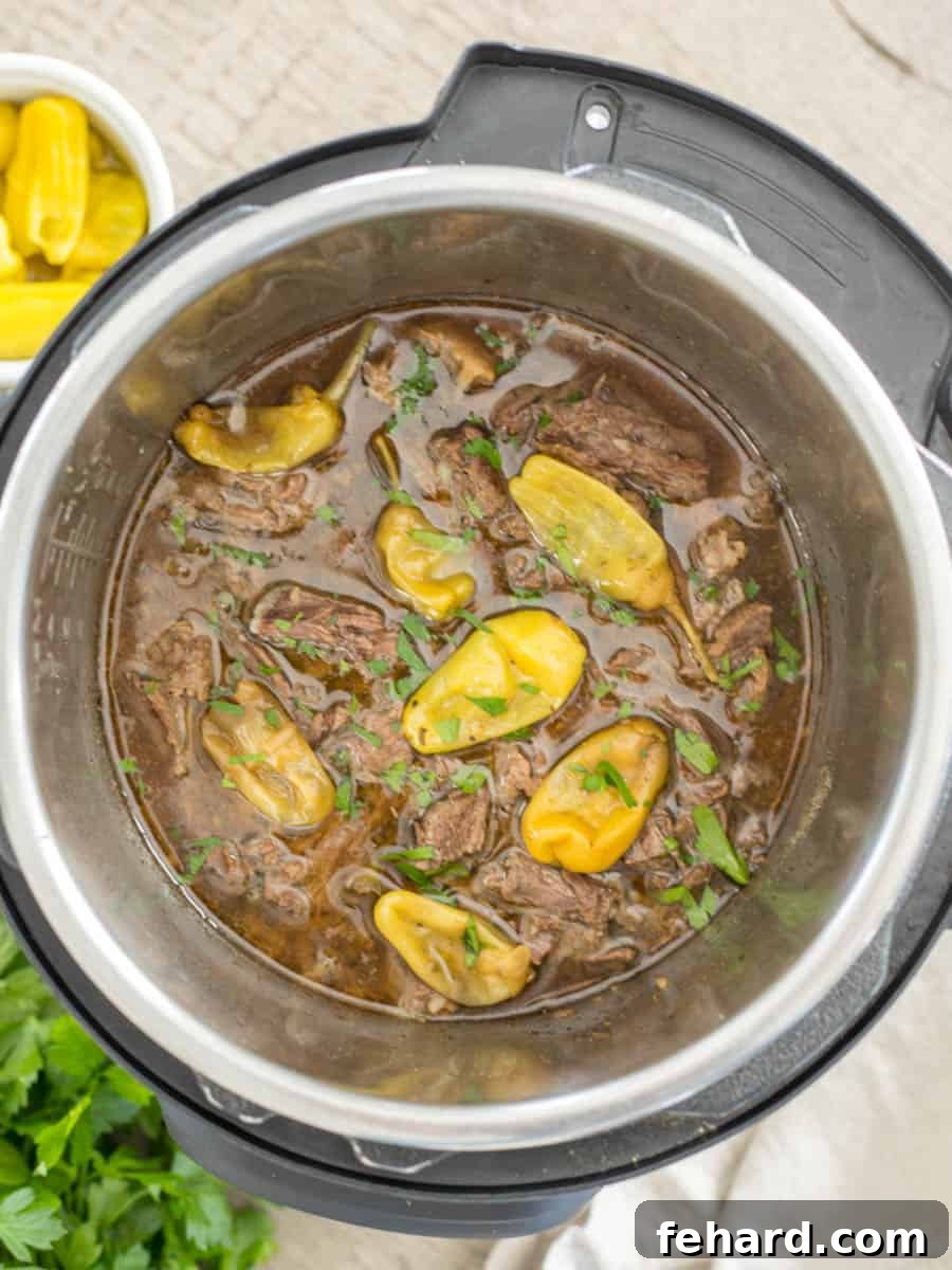 Cooked and shredded pot roast in inner pot of Instant Pot topped with Pepperoncini Peppers and parsley.