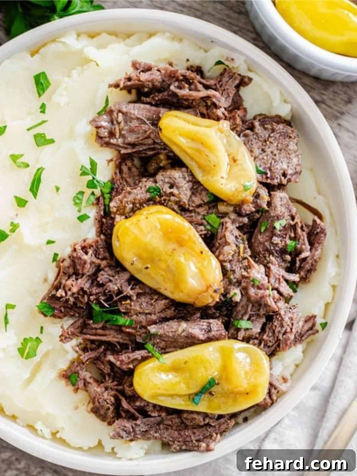 Instant Pot Mississippi Pot Roast dished up with mashed potatoes in serving bowl topped with minced parsley.