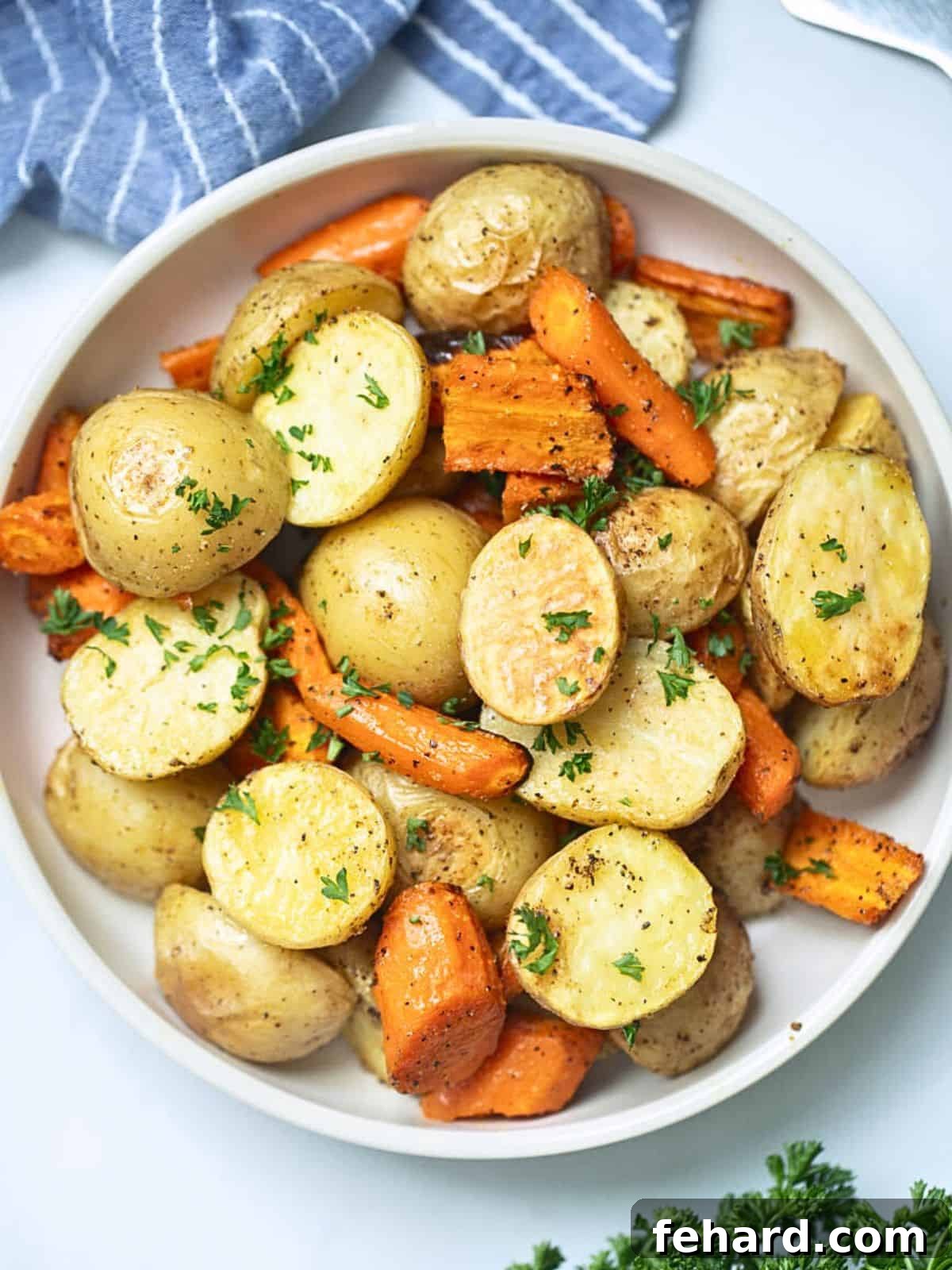 A white serving bowl filled with perfectly roasted potatoes and carrots, garnished with fresh parsley.