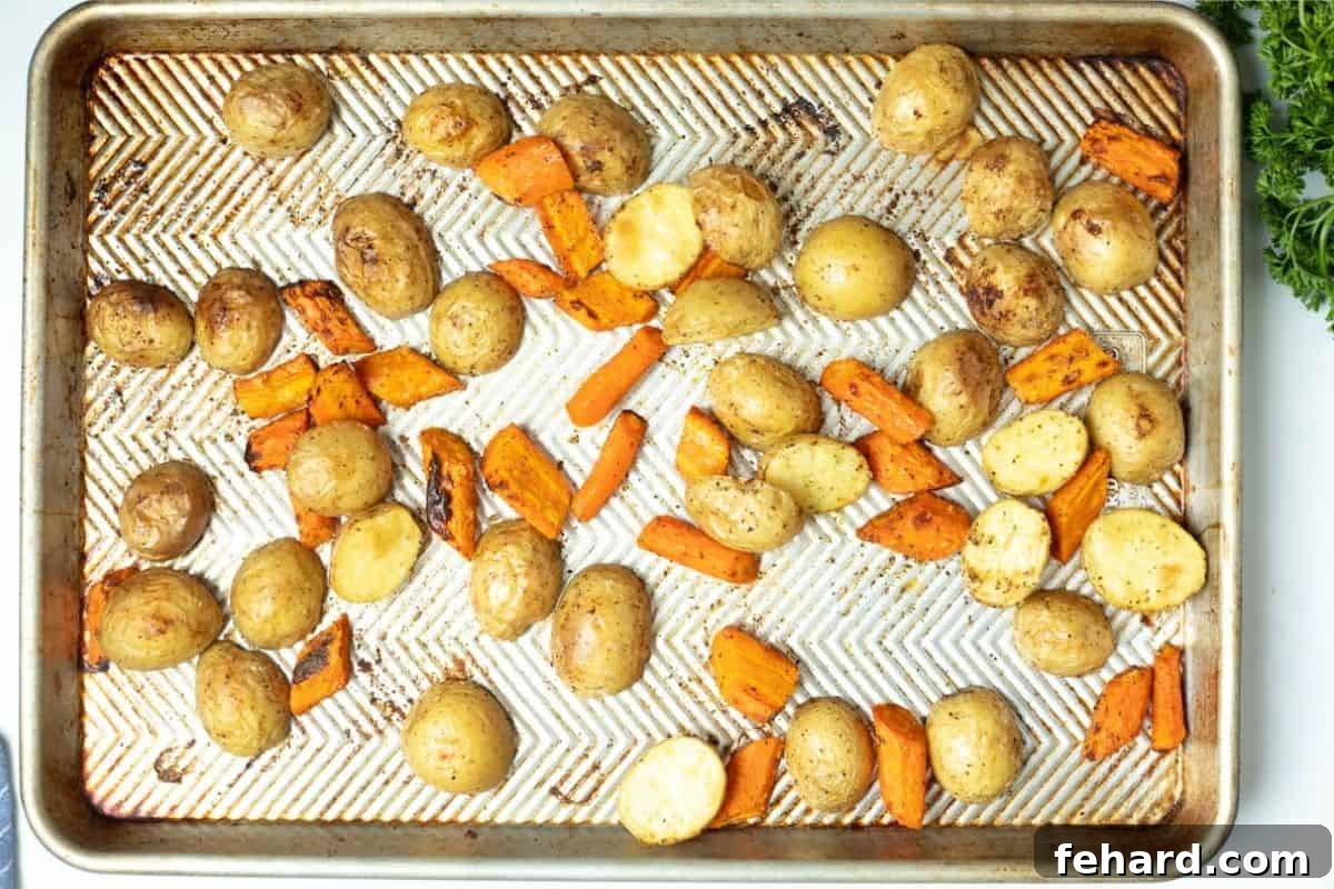 Perfectly roasted potatoes and carrots spread out on a sheet pan, ready to be served.