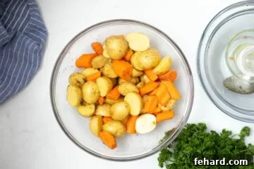 Mixing bowl with halved potatoes and carrots tossed with oil and salt and pepper.