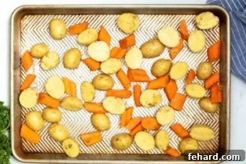 Seasoned potatoes and carrots spread out on sheet pan.