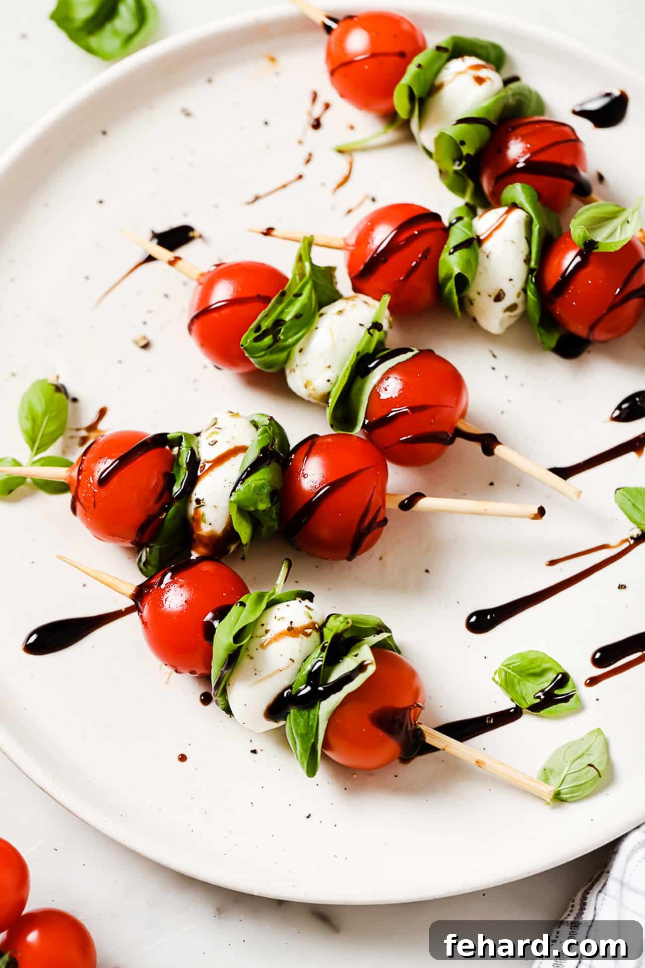 Fresh Caprese Bites 2 Caprese skewers drizzled with balsamic reduction on a white plate.
