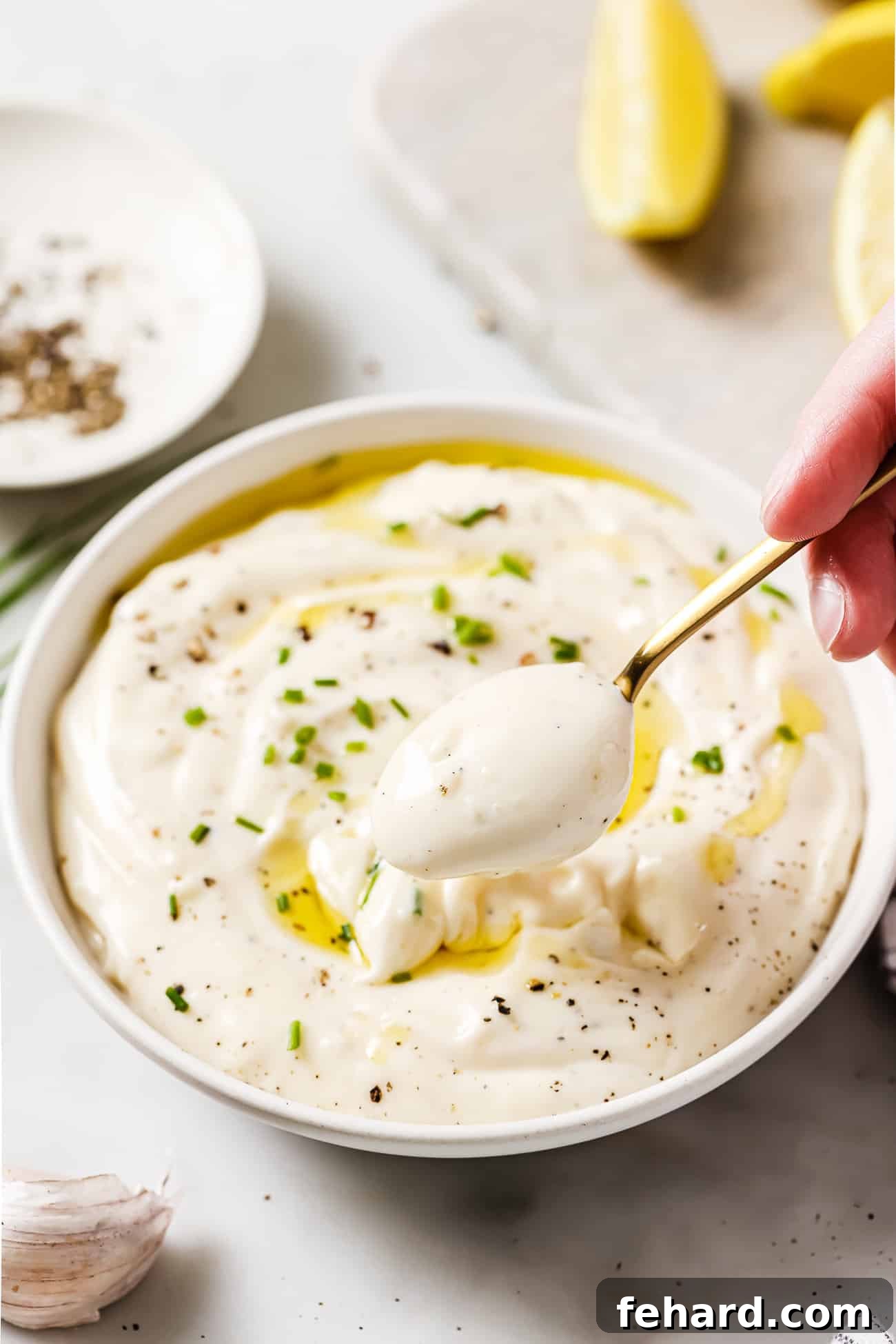 A large, rustic bowl filled with creamy garlic aioli, generously garnished with fresh green chives, presented against a natural background.