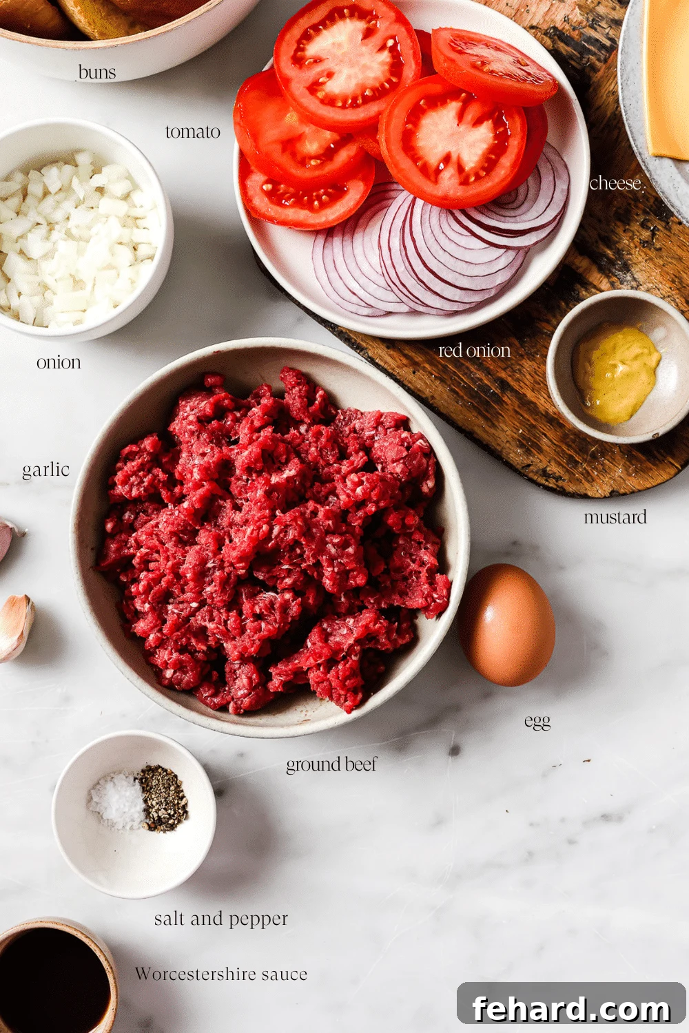 The Ultimate Homemade Burger 3 A curated display of fresh hamburger ingredients and vibrant toppings laid out on a clean white countertop, including ground beef, eggs, mustard, Worcestershire sauce, diced onions, garlic, lettuce, tomatoes, cheese, and buns.
