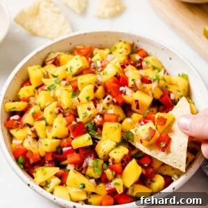 Close-up of freshly made mango salsa in a white bowl, showing diced ingredients and cilantro garnish.