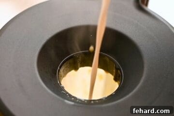 Warmed coconut milk being drizzled in steady stream through opening on blender to make homemade dairy-free eggnog.