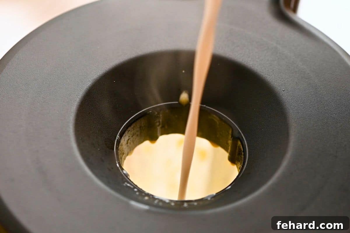 Warmed coconut milk being slowly drizzled in a steady stream through the opening on a blender lid to temper eggs for homemade dairy-free eggnog.