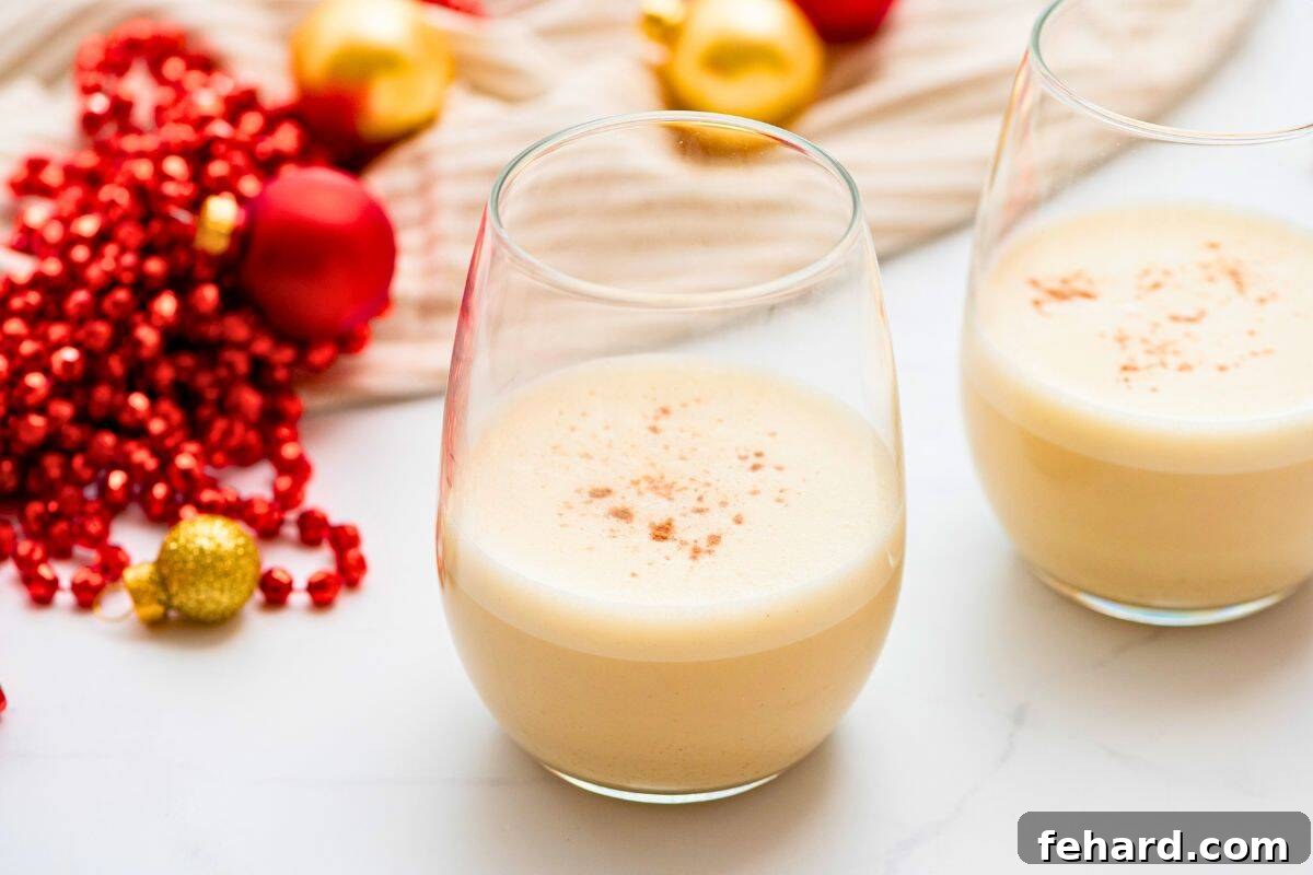 Two glasses of homemade dairy-free eggnog made with coconut milk and topped with grated nutmeg, presented beautifully with Christmas ornaments.