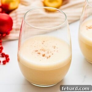 Homemade dairy free eggnog made with coconut milk in a glass mug sprinkled with grated nutmeg next to Christmas ornaments.