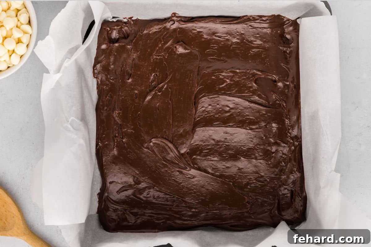 Melted chocolate layer of Christmas fudge spread out in parchment lined baking dish.