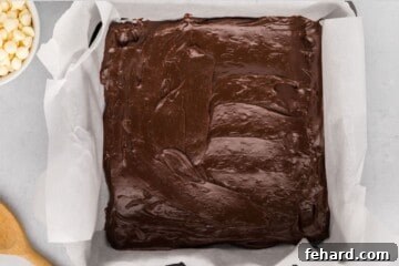 Melted chocolate layer of Christmas fudge spread out in parchment lined baking dish.