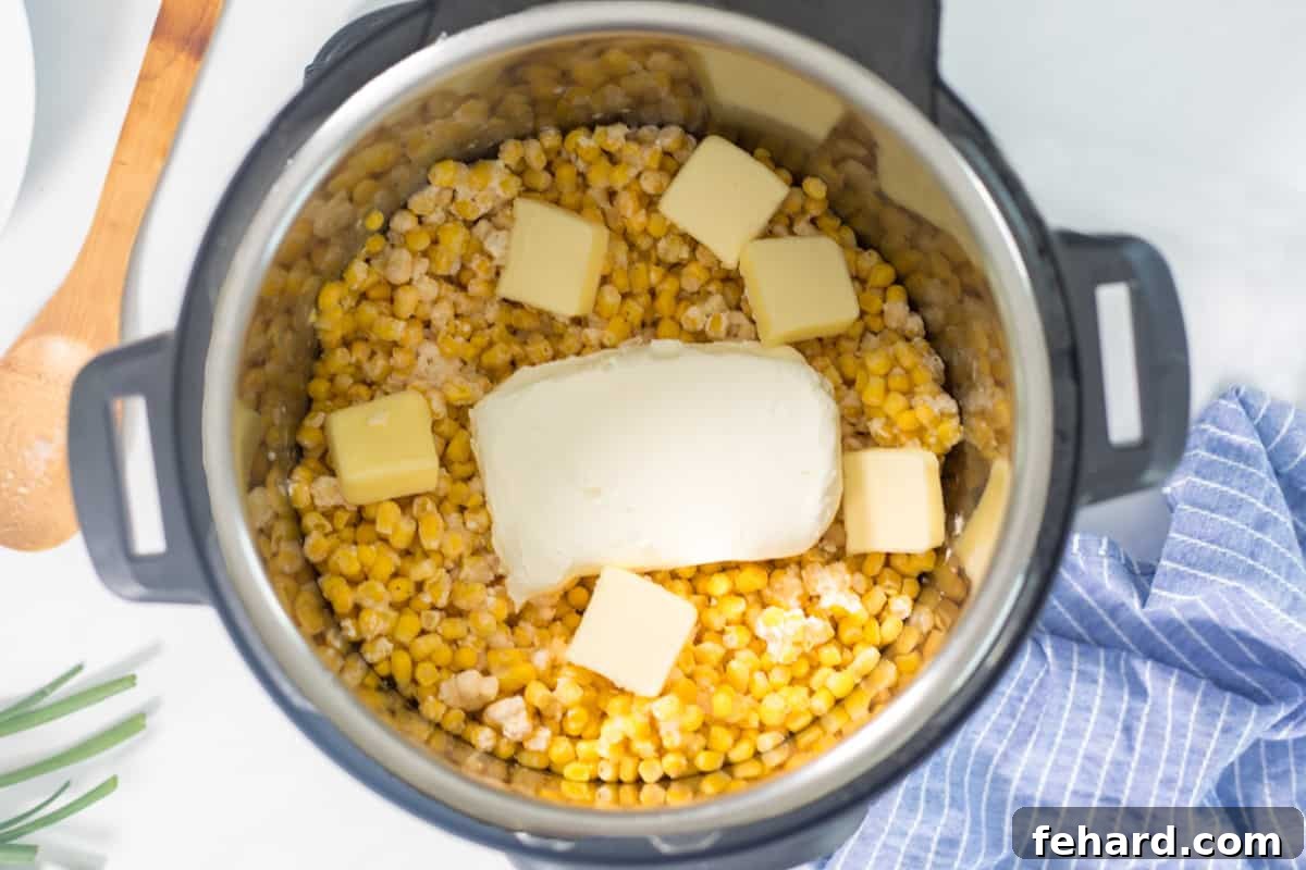 Instant Pot filled with broth, corn, heavy cream, cream cheese, and butter, ready for pressure cooking.