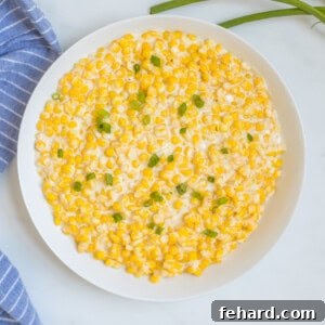 White bowl filled with Instant Pot creamed corn topped with green onions next to blue towel.