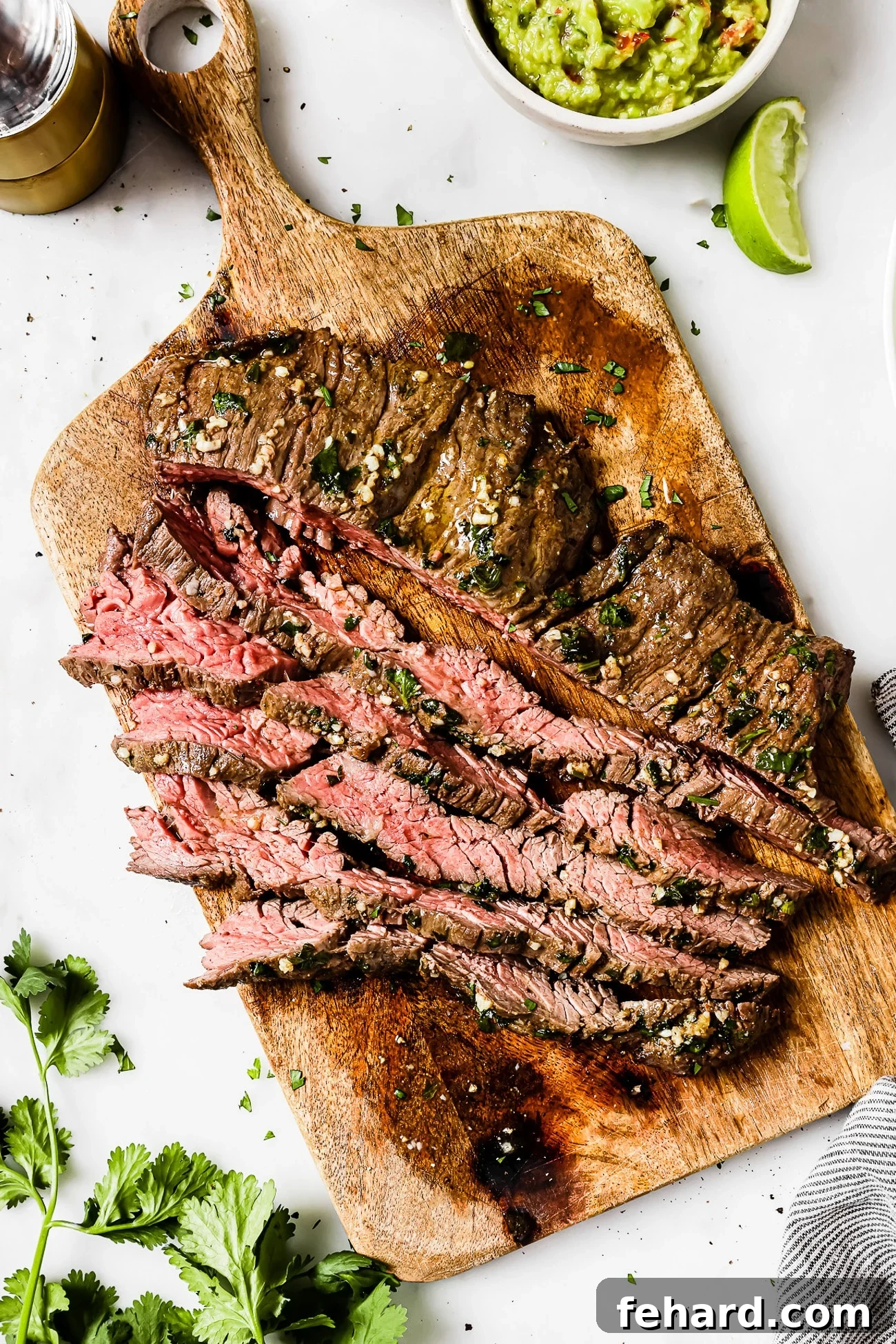 An overhead view of sliced carne asada on a wooden cutting board, perfectly cooked.