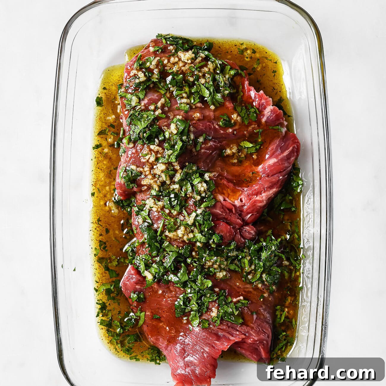 Marinated flank steak in a glass baking dish. 
