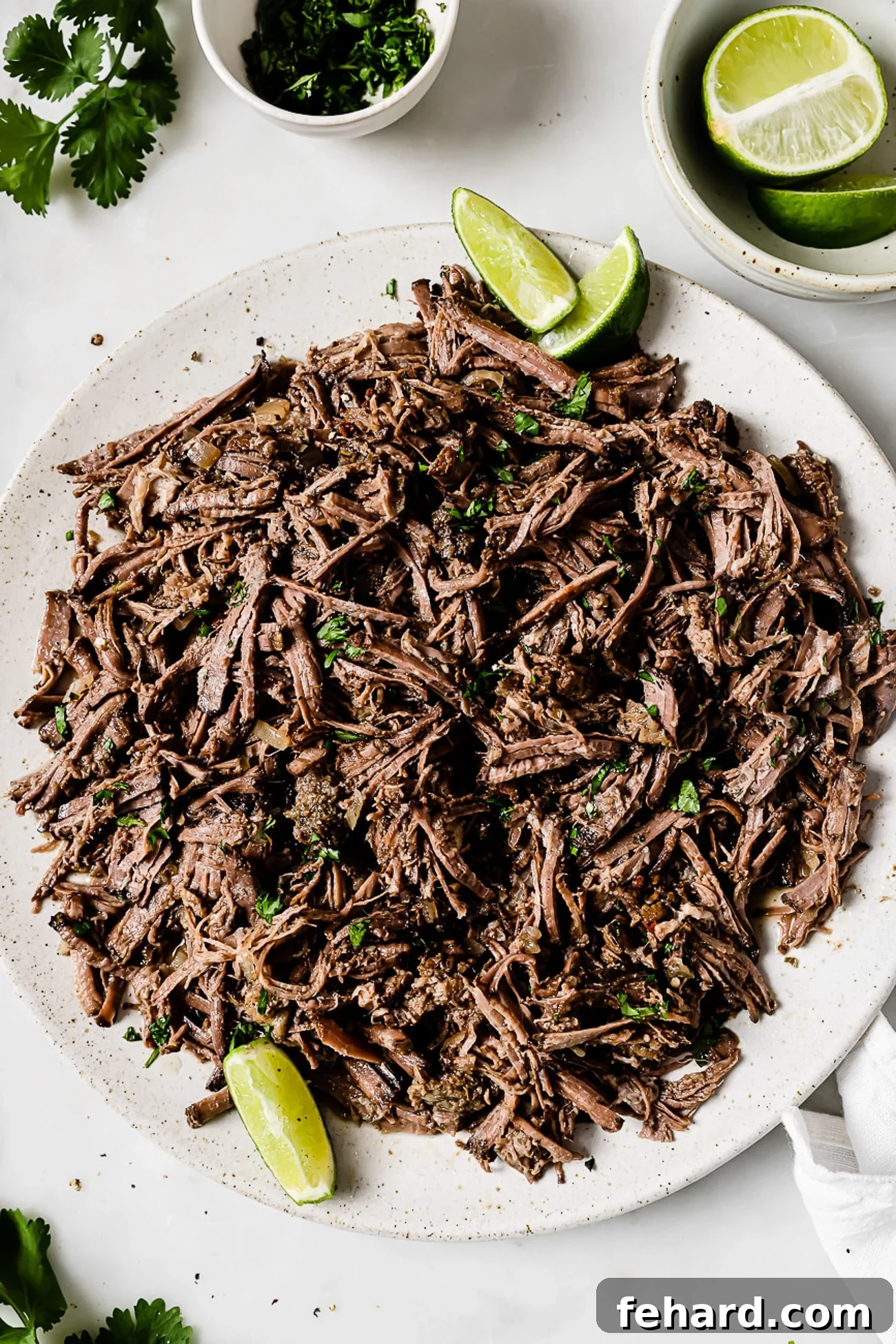 Slow-cooker barbacoa on a serving platter garnished with cilantro and lime wedges.
