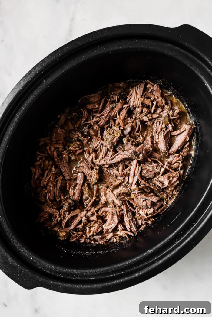 The shredded barbacoa is placed back in the crockpot.