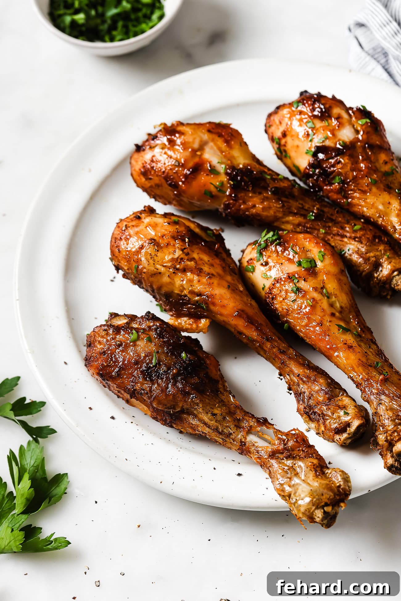 Five beautifully cooked chicken legs arranged on a white plate, ready to serve. 