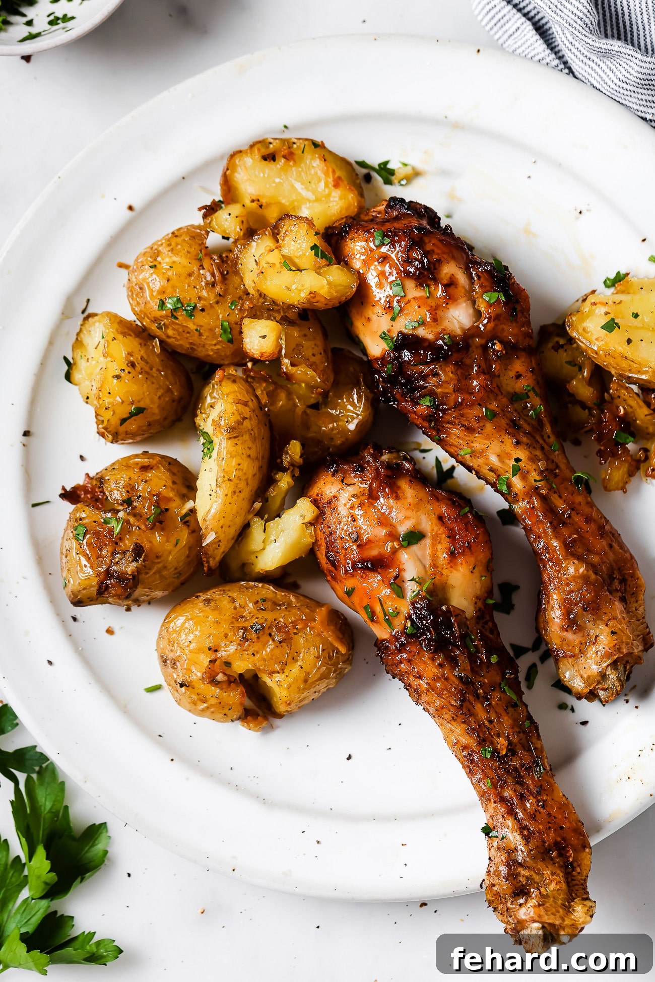 Two air fryer chicken legs and baby potatoes artfully arranged on a white plate, ready for a meal. 