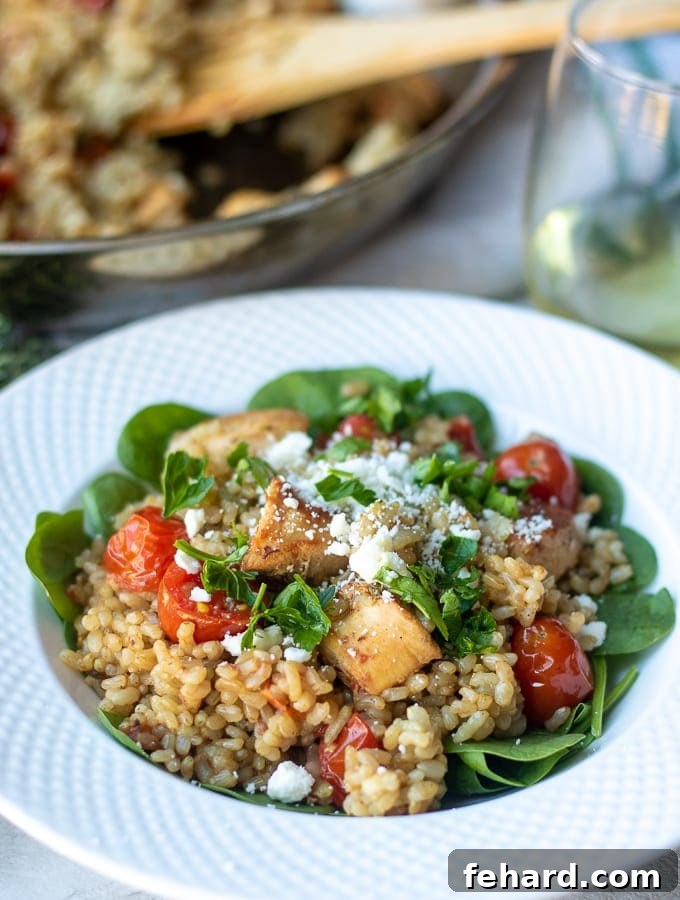 A delicious Mediterranean Chicken and Rice Skillet served in a white bowl, next to the cooking skillet.