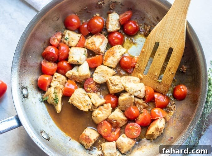 Chicken sautéed with vibrant grape tomatoes, minced garlic, and fresh herbs in a skillet.