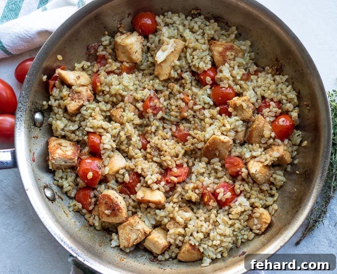 Chicken and rice simmering together in a large skillet, covered with a lid.