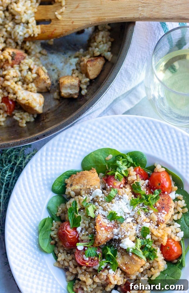 A skillet full of Mediterranean chicken and rice next to a white bowl showcasing the delicious finished dish.