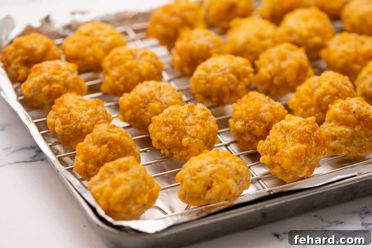 Freshly baked, golden-brown sausage balls resting on a wire rack over a foil-lined baking sheet.