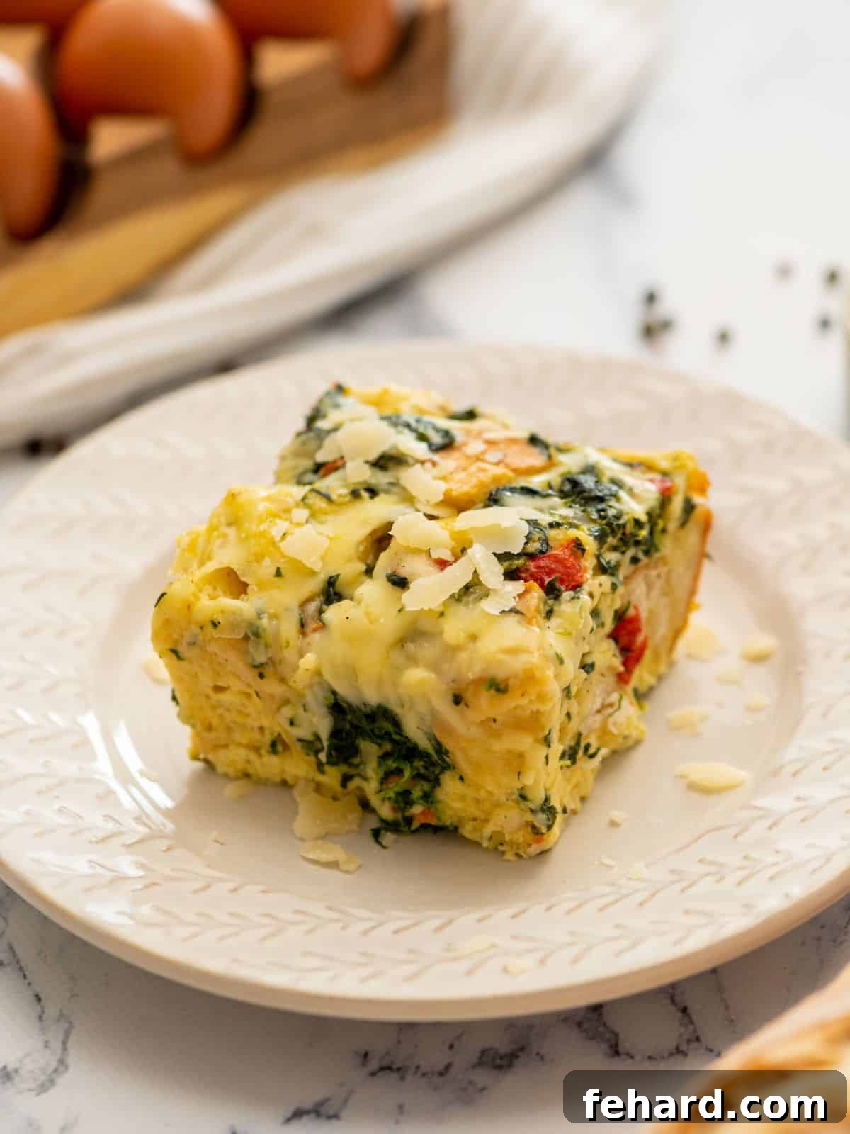Slice of spinach and cheese breakfast strata on white plate topped with shredded parmesan cheese.