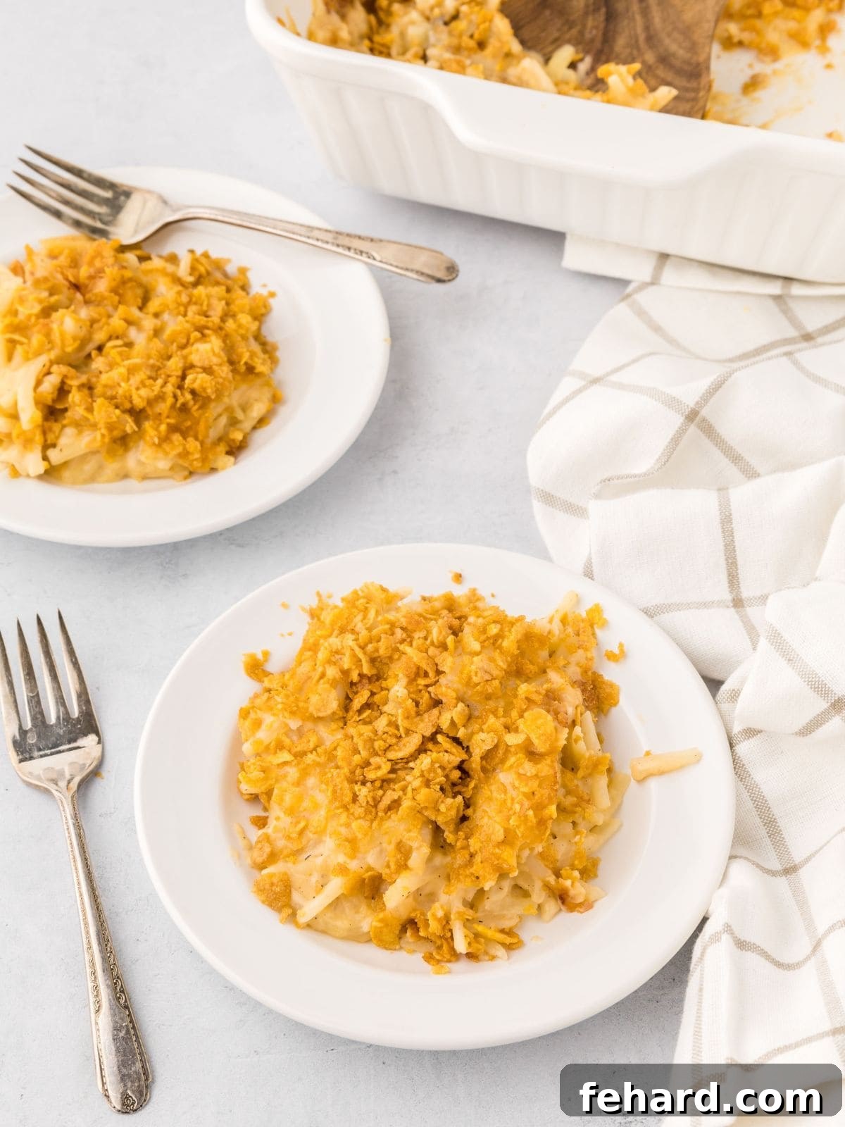 A serving of golden-brown Funeral Potatoes with a crunchy cornflake topping on a white plate, ready to be enjoyed with a fork.