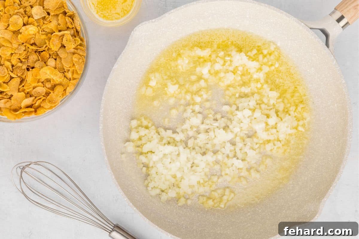 A sauté pan on the stovetop containing melted butter and finely minced onion, gently cooking until translucent.
