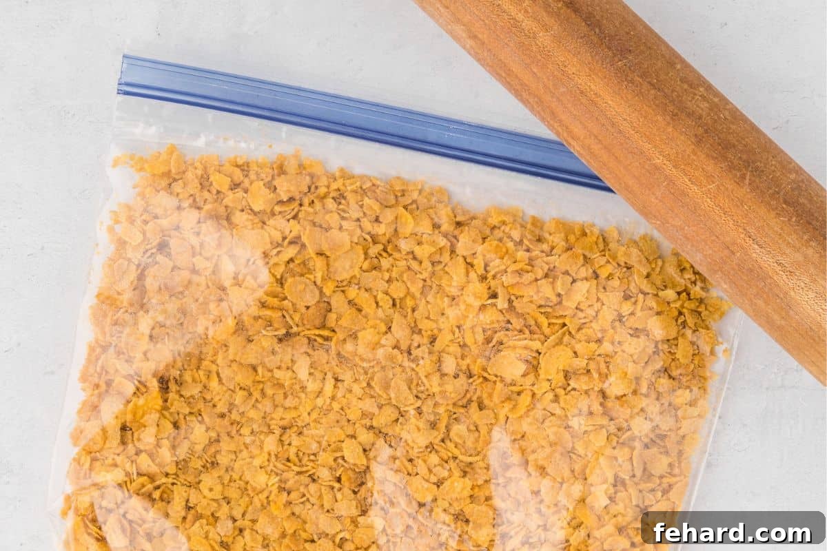 A clear plastic bag containing lightly crushed cornflakes, with a rolling pin resting nearby, illustrating the simple method for preparing the casserole's topping.