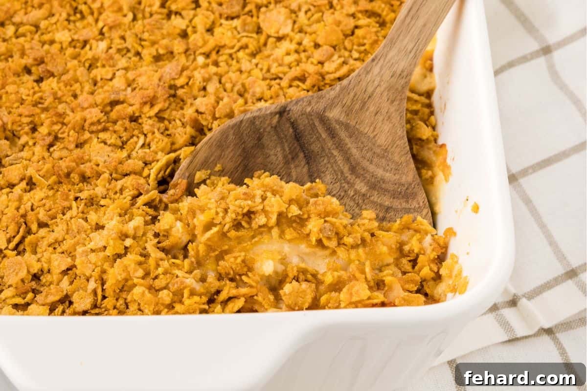 A wooden spoon dishing out a generous portion of hot, bubbly Funeral Potatoes from a large white baking dish, steam gently rising.