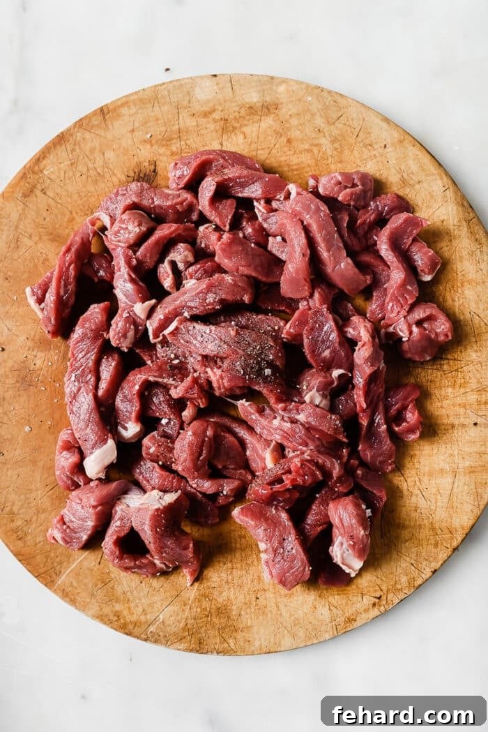 Melt-in-Your-Mouth Slow Cooker Pepper Steak 4 Seasoned sirloin strips on a wooden cutting board.