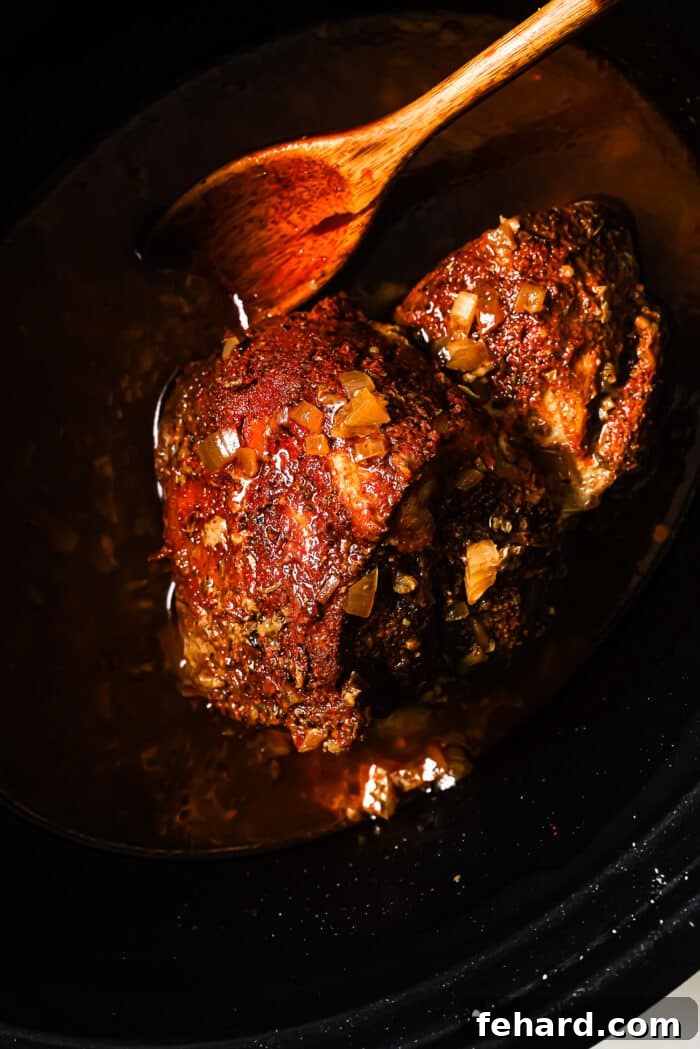 Melt-in-Your-Mouth Slow Cooker Pulled Pork 6 Cooked pork in a slow cooker with a wooden spoon in it.