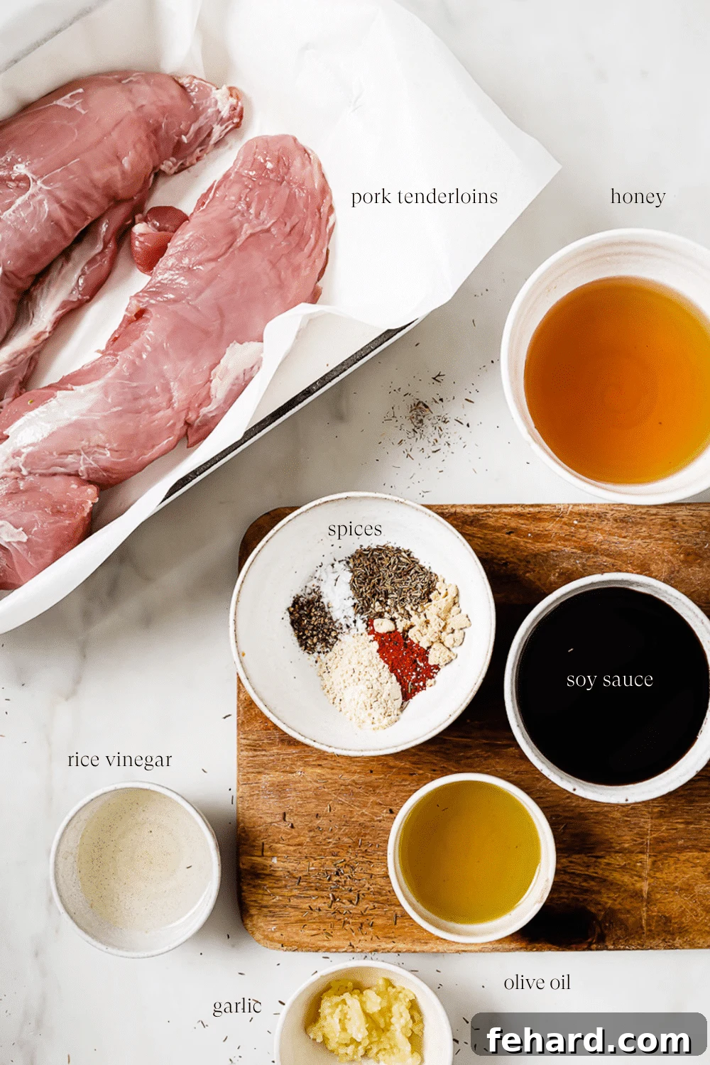 An inviting overhead shot of perfectly portioned and prepped ingredients for honey garlic pork tenderloin, neatly arranged on a pristine white countertop and a rustic wooden cutting board, showcasing freshness and readiness for cooking.