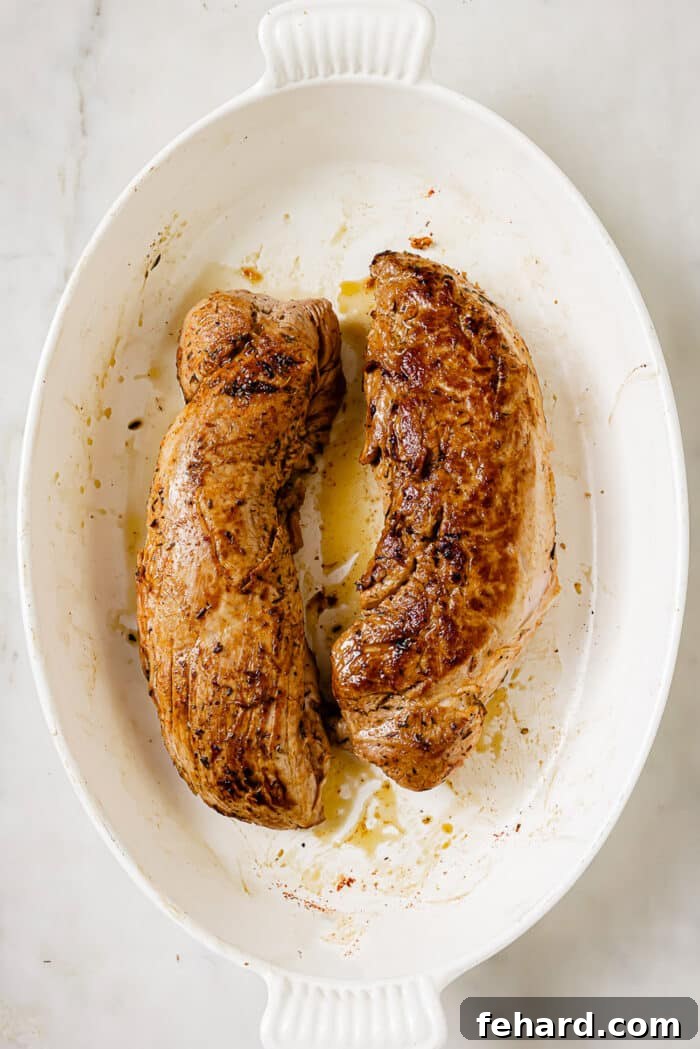 Two seared pork tenderloins, boasting a golden-brown crust, have been moved from the skillet to a baking dish, ready for the oven.