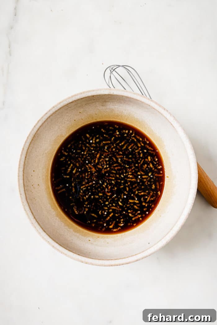 A small, clear glass bowl holds a rich, amber-colored honey garlic sauce, perfectly mixed, with a whisk resting on the side, ready to glaze the pork.