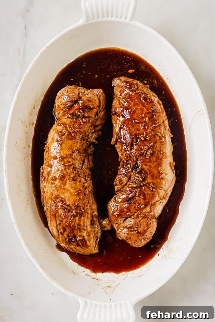 Two glistening pork tenderloins, generously coated in a shimmering honey garlic sauce, nestled in a baking dish, ready to be roasted to perfection.