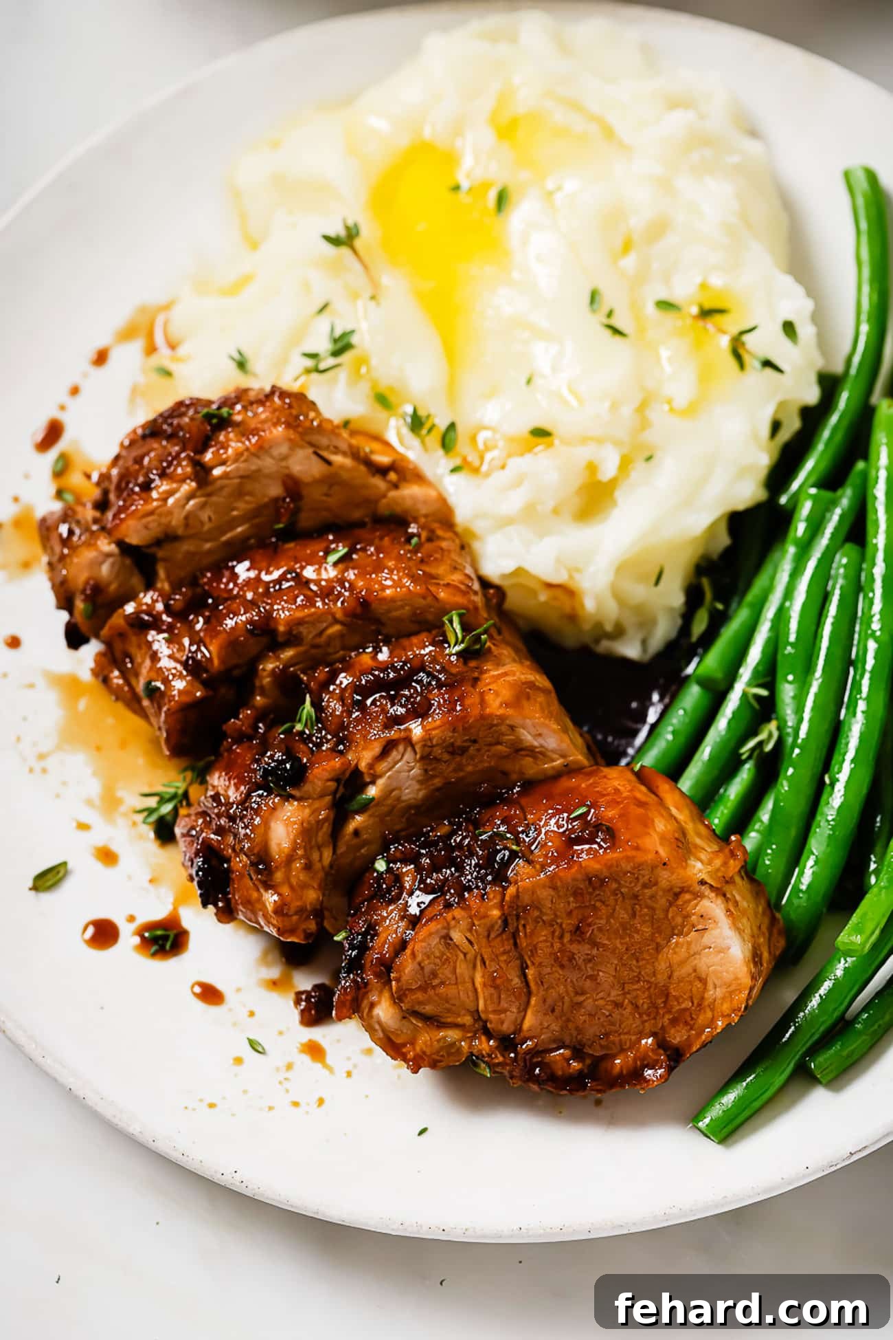 A vibrant and appetizing plate features perfectly sliced honey garlic pork tenderloin, accompanied by creamy mashed potatoes and crisp roasted green beans, showcasing a complete and balanced meal.