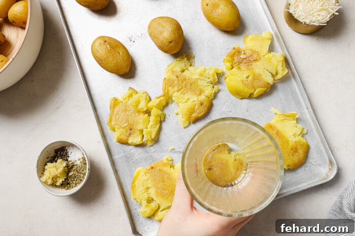 Crispy Smashed Potatoes 5 A hand gently pressing boiled baby potatoes on a baking sheet with the bottom of a glass, preparing them for smashing.