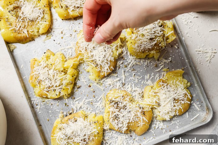 Crispy Smashed Potatoes 8 A hand adding a generous amount of freshly grated Parmesan cheese on top of the seasoned smashed potatoes.