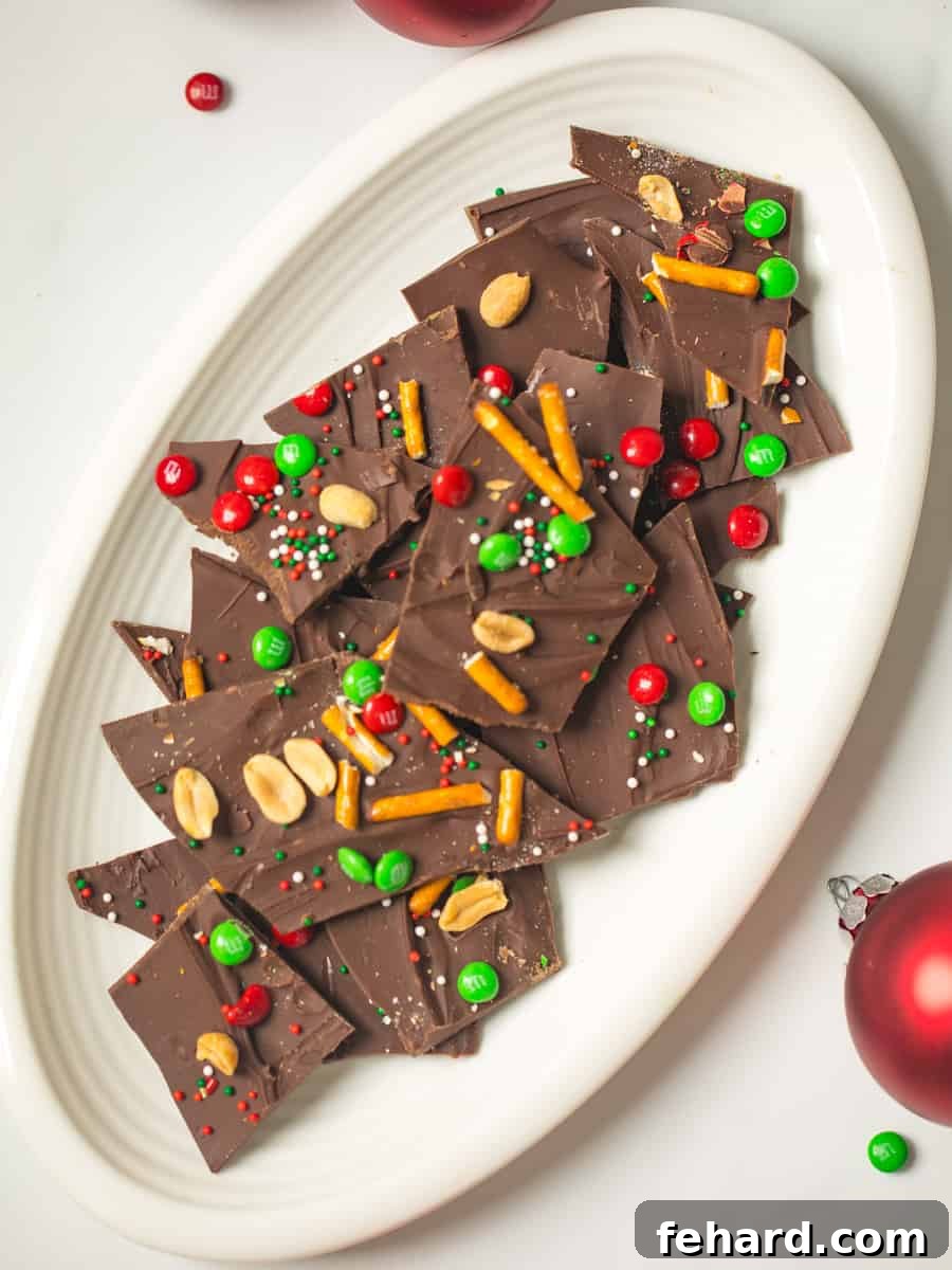 A vibrant plate of holiday chocolate bark featuring M&Ms, pretzels, nuts, and festive sprinkles.