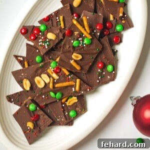 Plate of holiday chocolate bark topped with m&ms, pretzels, nuts, and sprinkles.