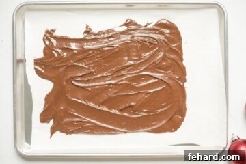 Smooth layer of melted chocolate spread on parchment paper on a baking sheet.