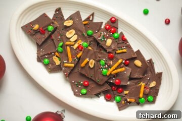 Plate of finished holiday chocolate bark topped with M&Ms, pretzels, nuts, and sprinkles.